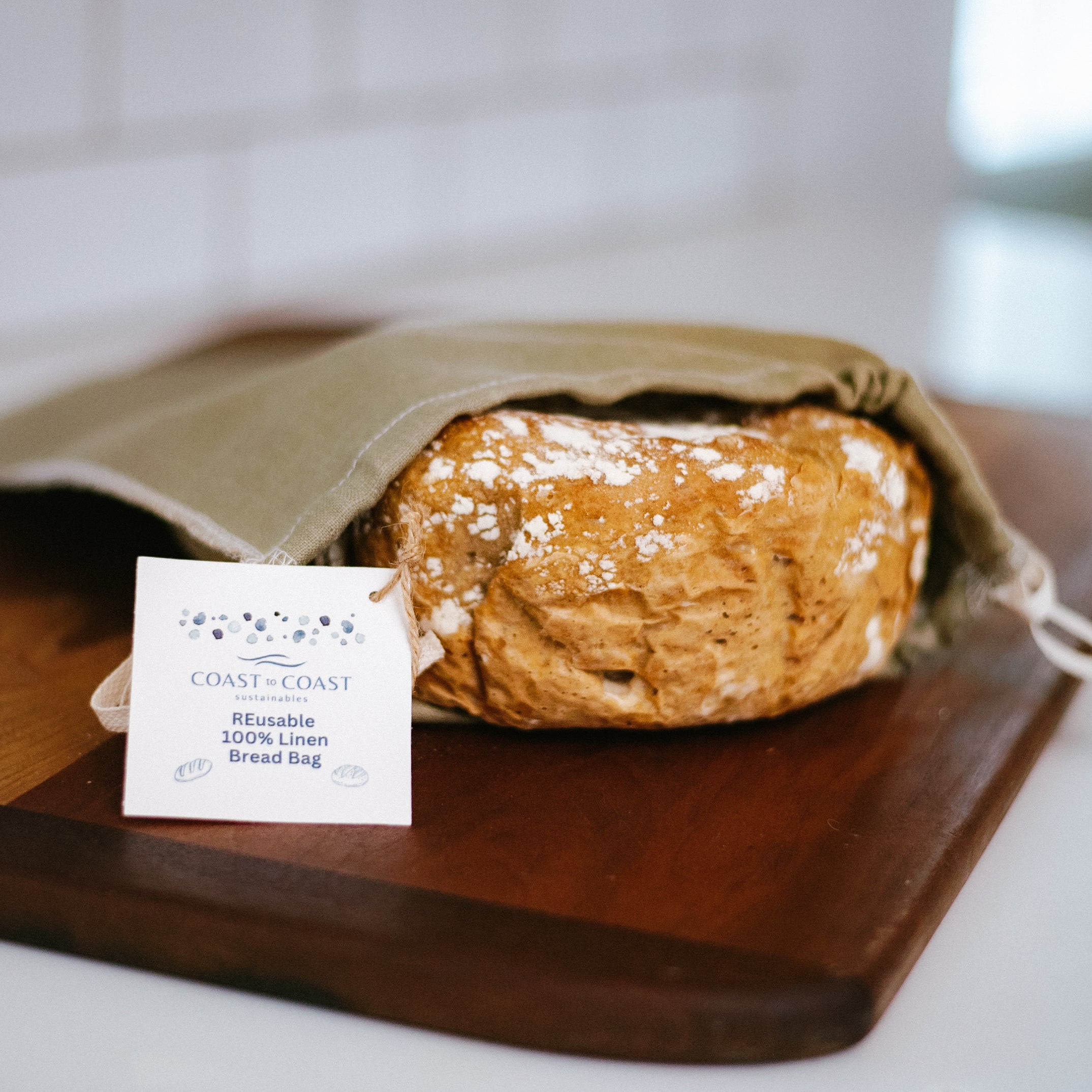 Loaf of bread in a linen bag on a wooden cutting board with a card in front