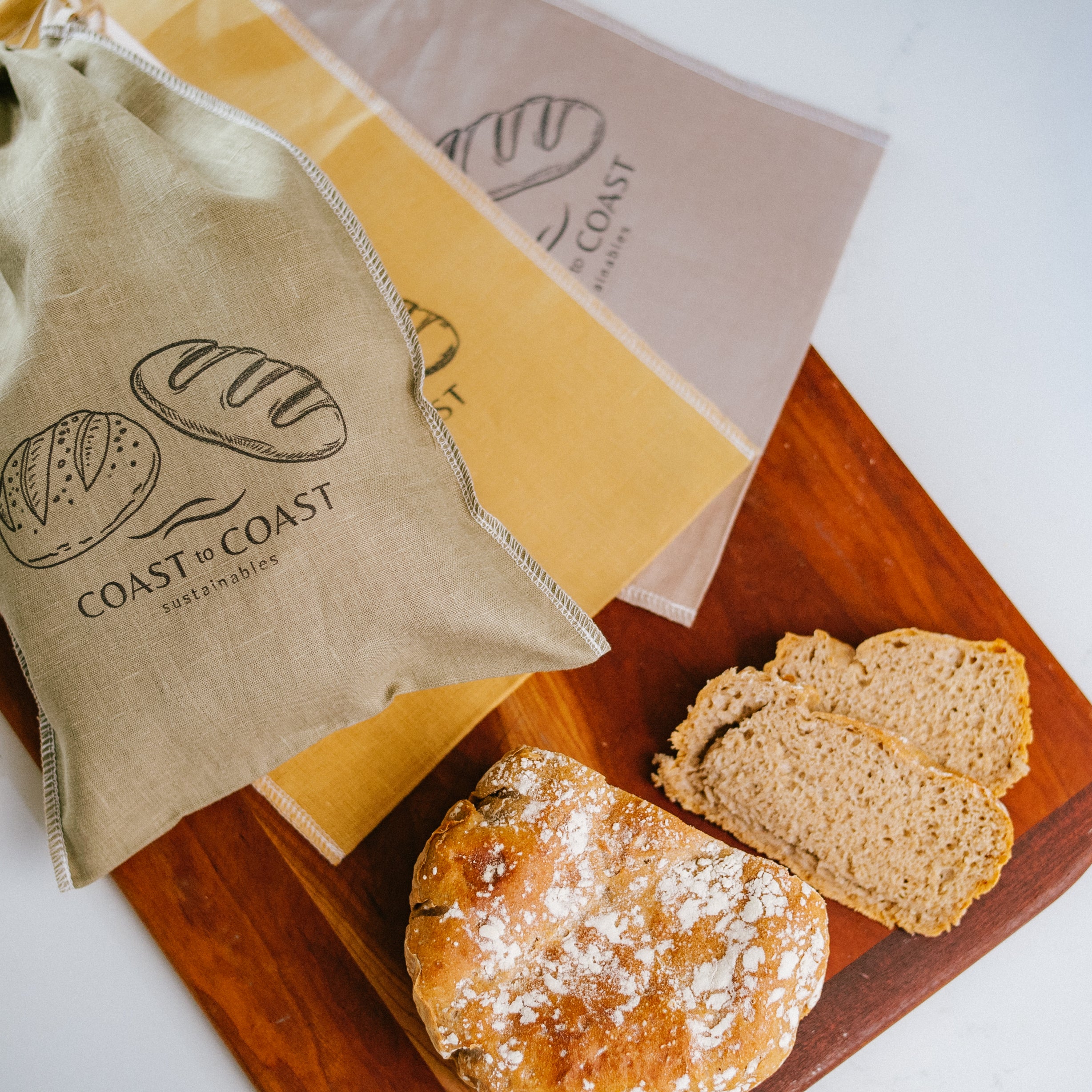 Bread on a wooden board with a 'Coast to Coast' branded linen bag and paper in the background.