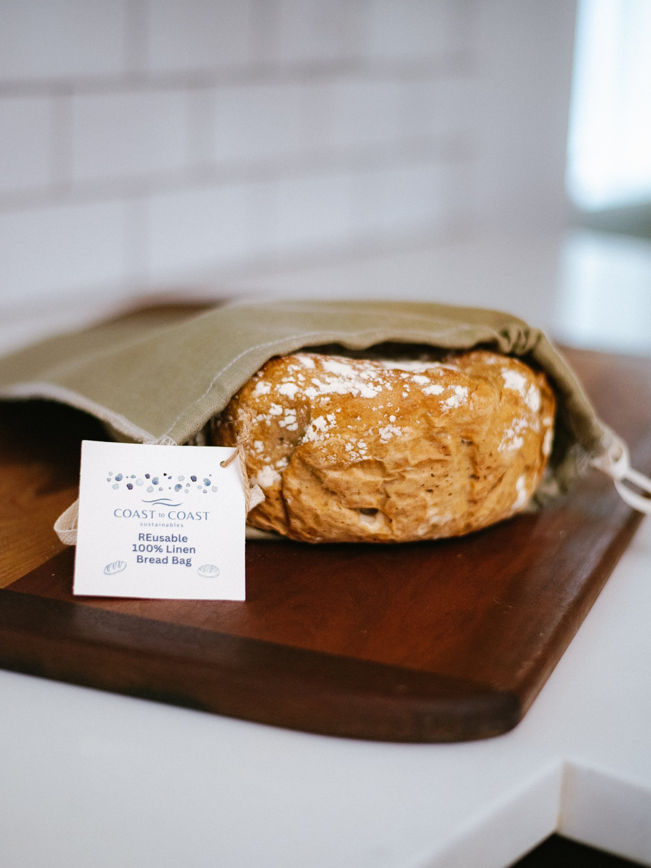 Loaf of bread in a linen bag on a wooden cutting board with a card in front