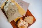 Bread on a wooden board with a 'Coast to Coast' branded linen bag and paper in the background.